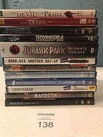 Photo showing stacked 12 DVDs including The Devil Wears Prada, The Queen, Terminator 3 & 2, Jurassic Park Ultimate Trilogy, Bond Die Another Day, The Bridge on the River Kwai, Hugh Grant collection, Caddyshack, Macbeth, Amadeus.