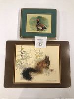 Two stacked table mats shown, one large with squirrel illustration and one smaller with duck illustration visible