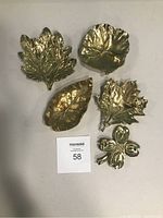 Top-down view of the 5 brass items showing 4 leaf-shaped dishes and 1 floral clip on a white background.