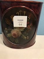 Side angle view of the lacquered wooden waste basket showing the floral motif on the front oval panel and the reddish lacquer finish.