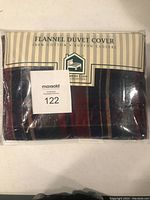 Packaged flannel duvet cover in plastic wrapping; label indicates 100% cotton and button closure, plaid pattern visible in navy and burgundy colors.