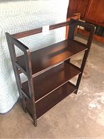 Side-angle view of the dark stained solid wood 3-tier folding bookshelf showing folding side frames and shelves.