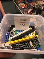 Top view of plastic bin with assorted Lego Technic parts, including beams in different colors and connector pins.