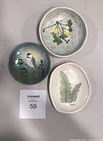 Top view of three small ceramic plates with different nature designs arranged on a white surface.