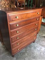 Frontal three-quarter view of cherry dresser showing five drawers with brass knobs and visible surface scratches.