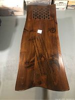 Top view of the wooden coffee table showing the chessboard inlaid near one end and the cribbage board carved into the surface below it. The table has a dark polished wood finish with visible wood grain and knots.