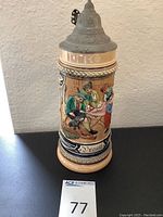 Front view of the 11 inch tall ceramic beer stein with detailed raised hand-painted scenes and pewter lid.