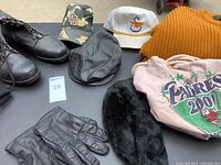 Top view of men's size 10 black leather boots, multiple hats, gloves, and clothing laid on a gray surface