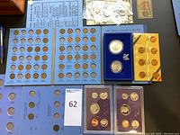 Photo showing coin albums with various slots for pennies and quarters, plus two proof sets in purple holders and loose coins