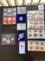 Top-down view of the coin sets and loose coins spread out on a black surface including various US coins and commemorative pieces.