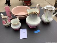 Five decorative pottery items shown together on table with visible pink teapot, green and white teapot, pink floral pitcher, small white pot, and pink vase.