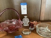 Overview of all six glass items on wooden surface including pink basket, clear bottle, red shot glass, pink sectioned dish, candle holder, and clear paperweight.