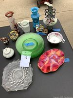 Full lot display showing green Depression glass plates, ceramic figurines of animals, a floral teacup, and various tall vases including an Asian bird vase with a chip.