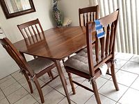 Dining table with four matching wooden chairs in tiled room, showing full set from angled side view.