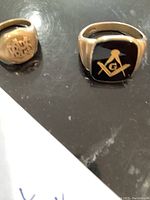 Both rings on a dark surface showcasing Masonic emblem and monogram