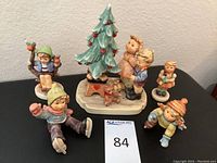 Seven Hummel Goebel Germany hand-painted ceramic figurines including a Christmas tree 8 inches tall, children, and teddy bear.