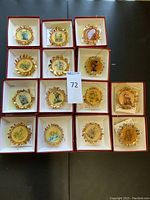 Overhead shot of 15 gold Hummel Christmas ornaments, each in a red-lined box arranged in groups of five across three rows.