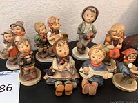 Photo showing entire set of nine Hummel West German statues arranged on a black surface.