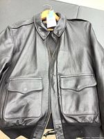 Front view of men's dark brown leather jacket on hanger, showing two flap pockets and zipper