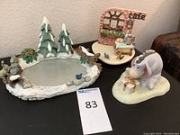 Photo showing the skate rink figurine with pine trees, squirrels, and birds, alongside the cafe resin scene and donkey gift figurine.