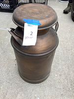 Full view of the tall cylindrical solid metal milk jug with a rounded lid and attached handle, showing its approximate size.