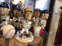 Multiple Padres bobbleheads with players wearing white uniforms and blue caps, alongside collectible baseballs and Randy Jones statue.