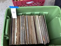 Top-down view of numerous record albums in a green plastic crate, showing their spines and edges, some wear visible.