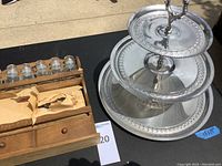 View of wooden spice rack with glass jars and metal lids beside three-tiered metal plate stand with rooster handle.