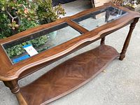 Full view of wood and glass console table showing two glass inset panels on top, carved wooden edges, turned legs, and lower shelf with patterned veneer.