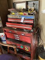 Full view of the vintage red metal rolling toolbox with smaller metal toolbox on top and various tools visible inside drawers and openings.