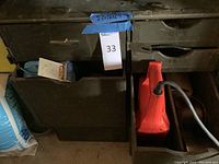 Black toolbox closed with metal latch, positioned next to a red power tool (reciprocating saw)