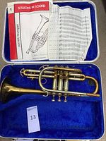 Trumpet in case lined with royal blue velvet next to a music book opened to notes and exercises.
