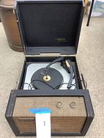 Open portable phonograph showing turntable, tonearm, and front control panel with knobs