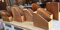 Photo showing 11 handmade solid wood magazine holders arranged on table, varying sizes and shapes.