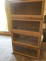 Four wooden stackable display cabinets with glass front doors assembled vertically, showing all four units stacked and doors closed.