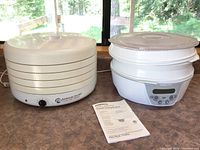 Side view photo showing American Harvest Classic Food Dehydrator with dial control and Presto Food Dehydrator with digital panel, both assembled with lids, sitting on a counter.