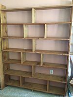 Front view of large handcrafted pine wood bookcase showing asymmetrical geometric shelves and natural wood finish.