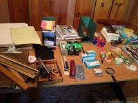 Photo showing wide view of assorted office supplies on a wooden table, including rulers, legal pads, scissors, stapler, tape dispensers, batteries, hole puncher, and other small items.