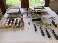 Overview of all painting supplies on table including rollers, trays, scrapers, and cans