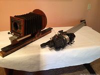 Wide shot showing the vintage accordion camera mounted on its wooden stand and the additional camera equipment next to it on a white table.