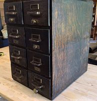 Angled side and front view of the dark stained wooden index holder showing the set of 8 drawers with metal handles and label slots. Visible wear on the wood surface and drawer handles.