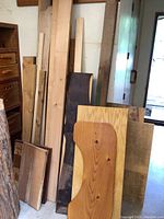 Various sizes of hardwood and softwood planks and sheets stacked vertically in corner, showing different wood textures and finishes