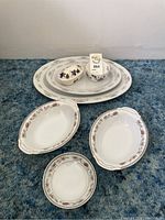 Photo showing assortment of china platters and serving bowls arranged on carpet; varied sizes; floral and gold trim patterns visible; crazing observable on some pieces