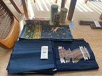 Photo showing two navy blue cushion covers and the folded tablecloth with floral and animal patterns spread on the floor.