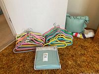 Photo showing multiple colorful Japanese-style hangers in pink, yellow, green, blue, and metallic finish, alongside a folded pastel green duvet cover in packaging, and other folded household textiles.