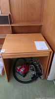 Full view of the wooden Ikea Anton desk closed with the vacuum cleaner underneath it, showing its compact size and wooden finish.
