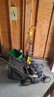 Side view of Murray gas lawn mower, Weed Eater electric trimmer, and green Scotts seed spreader in garage setting.