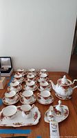 Overview showing 12 tea cups with 12 saucers, teapot, sugar bowl, creamer and tray on wooden table