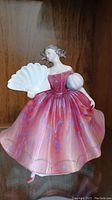 Front view of Royal Doulton First Waltz figurine, showing detailed facial features, pink floral dress, and large white fan held in raised right hand.