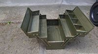 Open fold out green metal toolbox showing four tiered compartments on both sides and central storage section.